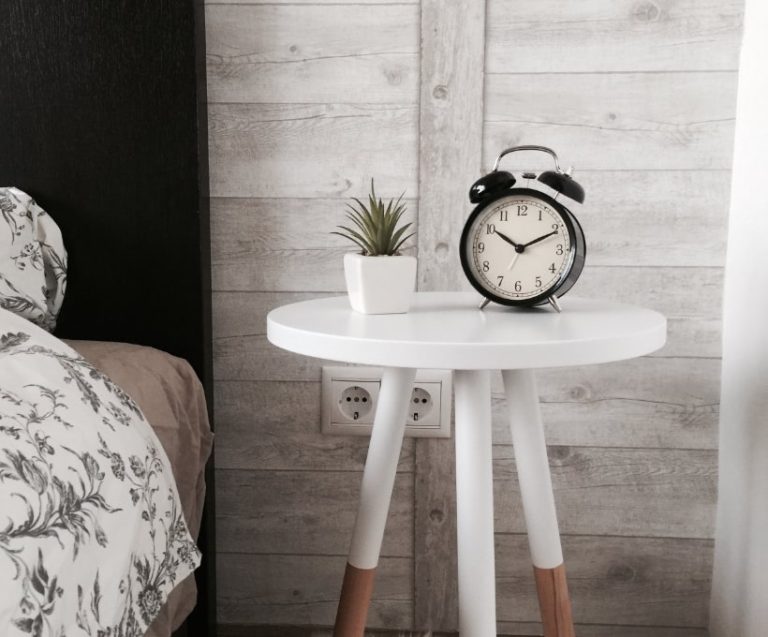 床邊白色長腳小圖桌上有一時鐘和小盆栽